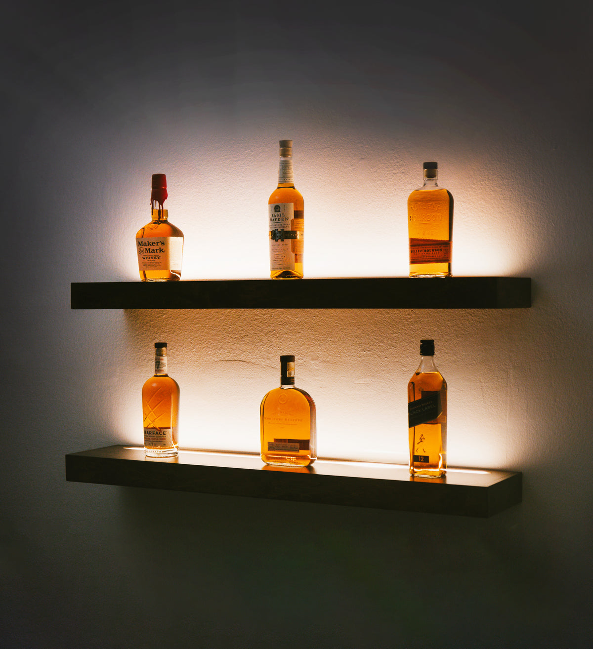 Two wooden shelves mounted on a wall, with LED strips used for lighting, displaying bottles of whiskey.
