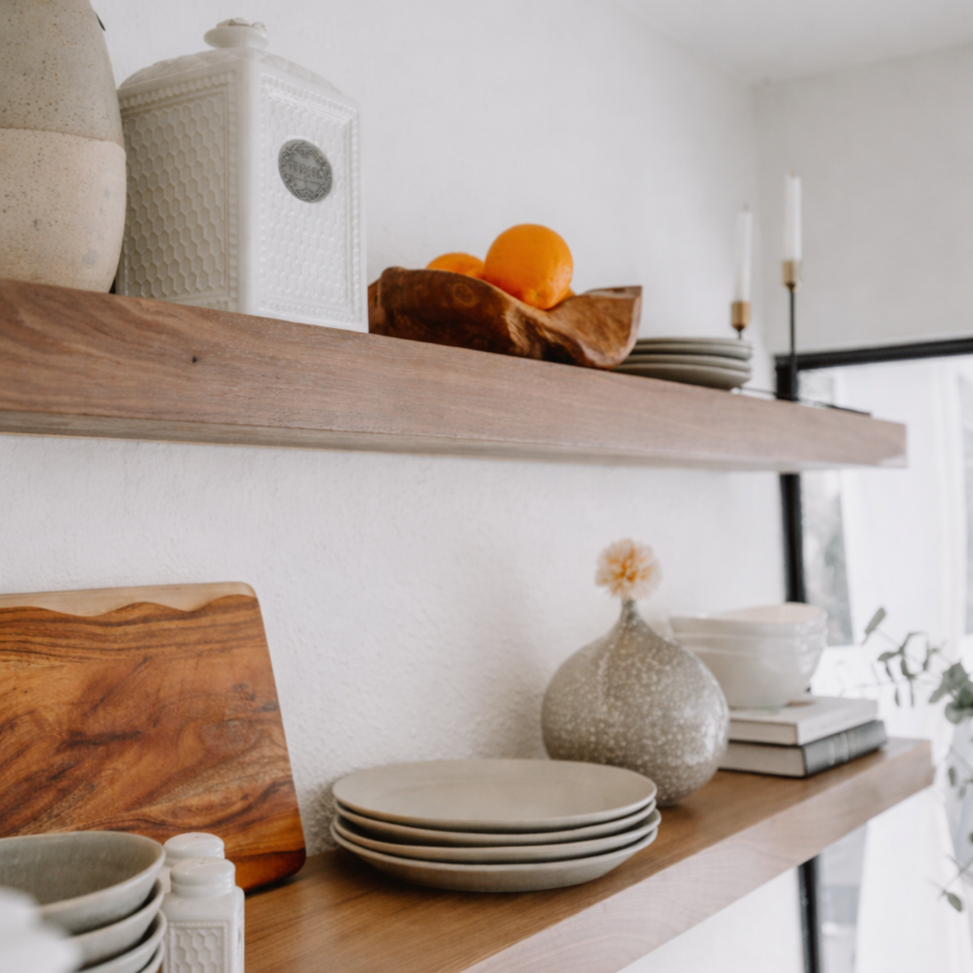Wooden shelves with ceramic plates, a wooden cutting board, and decorative items in a kitchen.