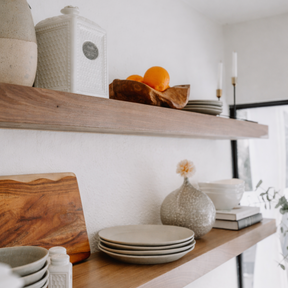 Wooden shelves with ceramic plates, a wooden cutting board, and decorative items in a kitchen.