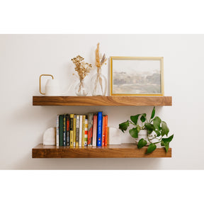 Wooden shelves with books, a vase with dried flowers, and a framed picture against a white wall.